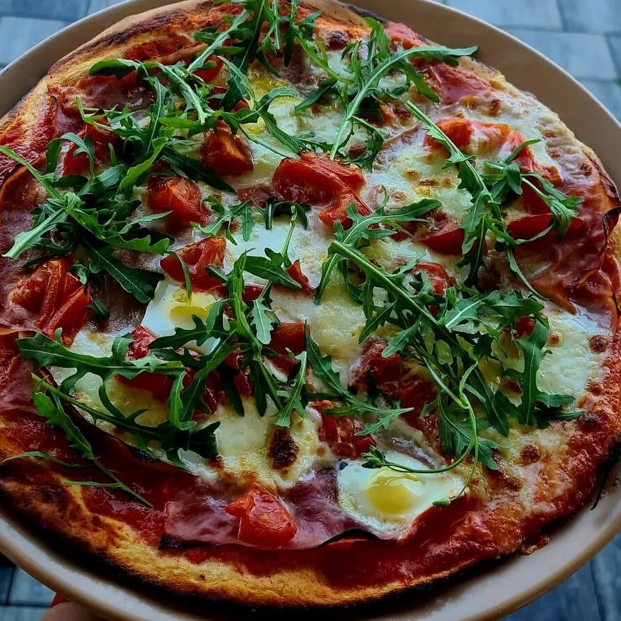 Pizza à la roquette, aux tomates, au jambon et à l’œuf au plat dans une assiette